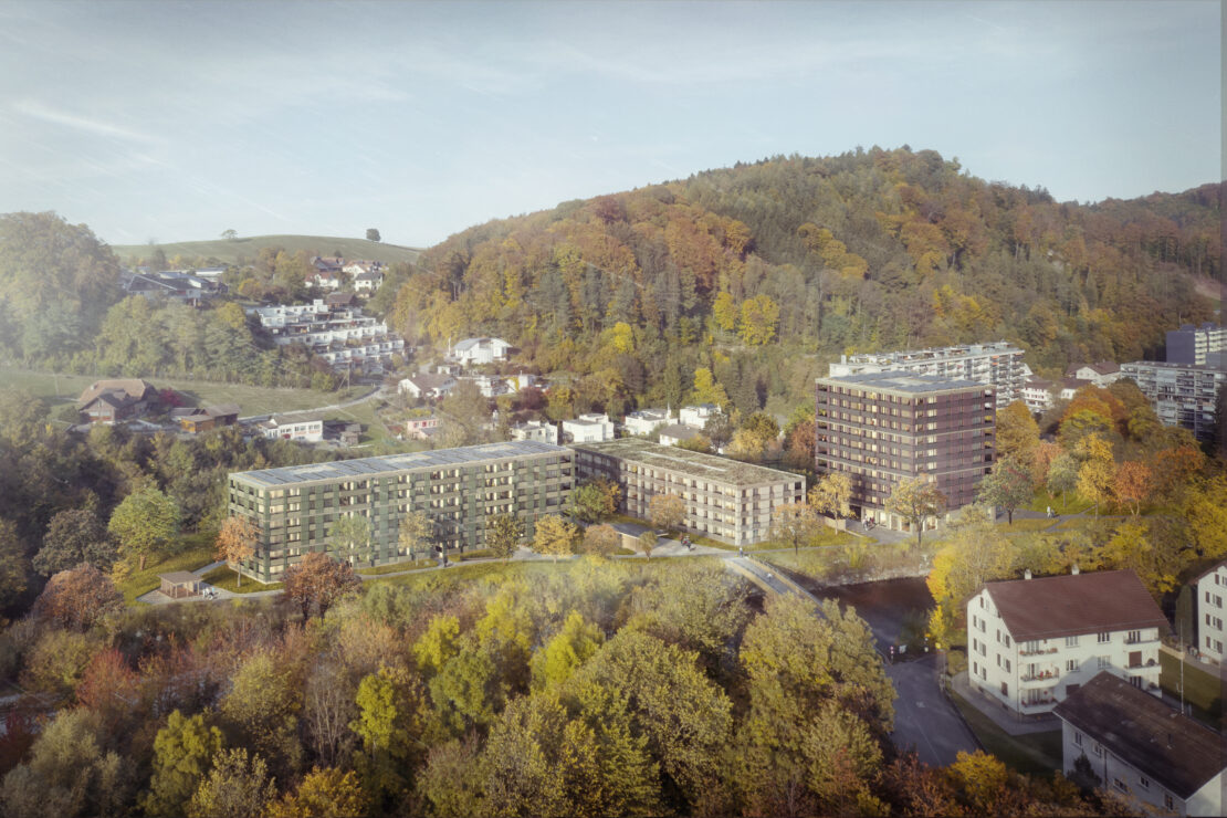 Luftaufnahme moderner Wohnhäuser, umgeben von herbstlichen Bäumen und grünen Hügeln. Die Landschaft zeigt eine Mischung aus Wohnhäusern, mit einigen Strassen und Häusern, eingebettet in das Laub, vor der Kulisse bewaldeter Hügel.